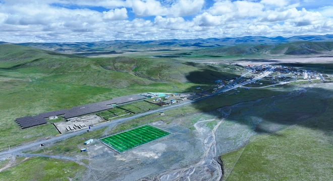 Vista a&eacute;rea de una microrred solar fotovoltaica junto a un pueblo remoto de alta monta&ntilde;a, rodeado de praderas y monta&ntilde;as