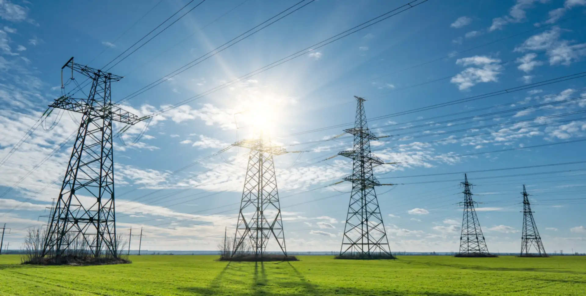 Torres de transmisi&oacute;n entre campos verdes bajo un sol radiante
